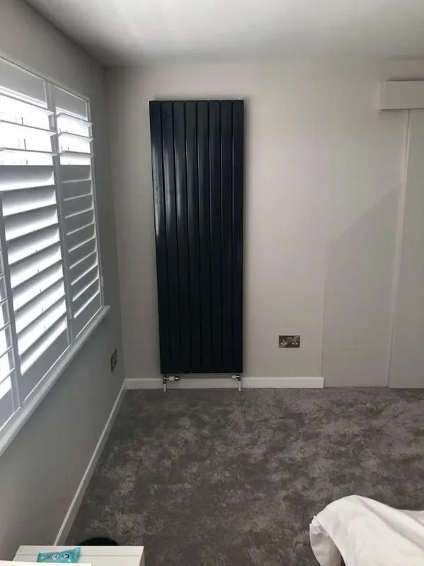 Tall black designer radiator fitted in a bedroom